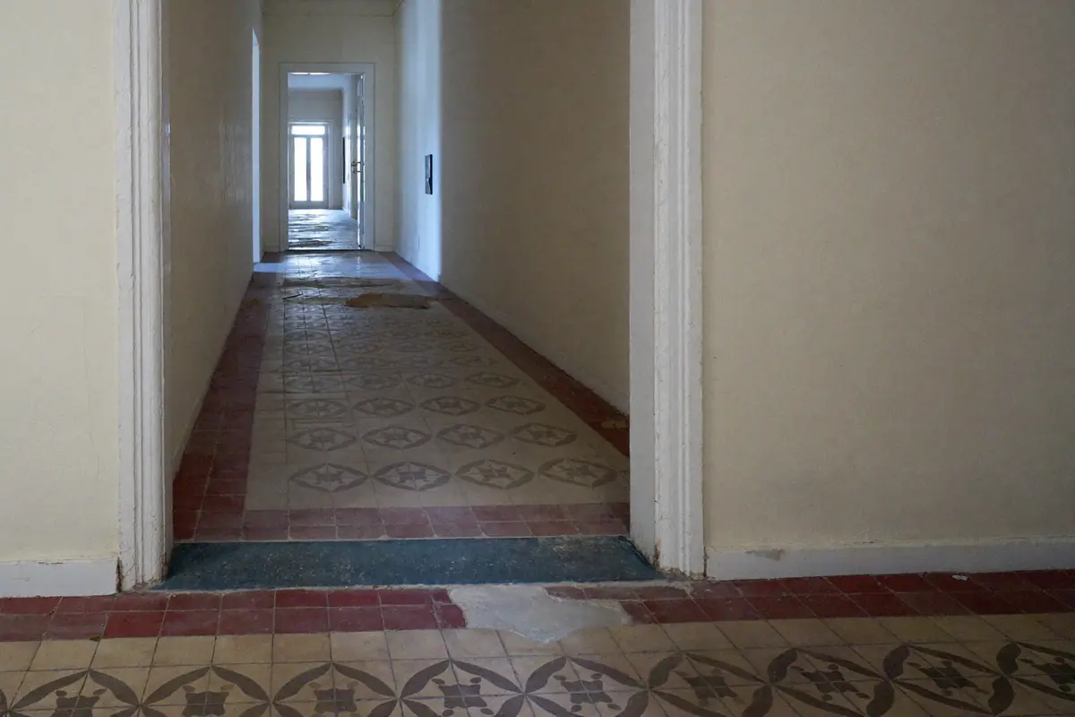Lange gang van een oud stadspand met een versleten vloer van cementtegels met patroon en een rode tegelrand